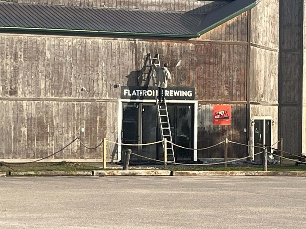 Flatiron Brewing sign above door of weathered wooden building, person on ladder.