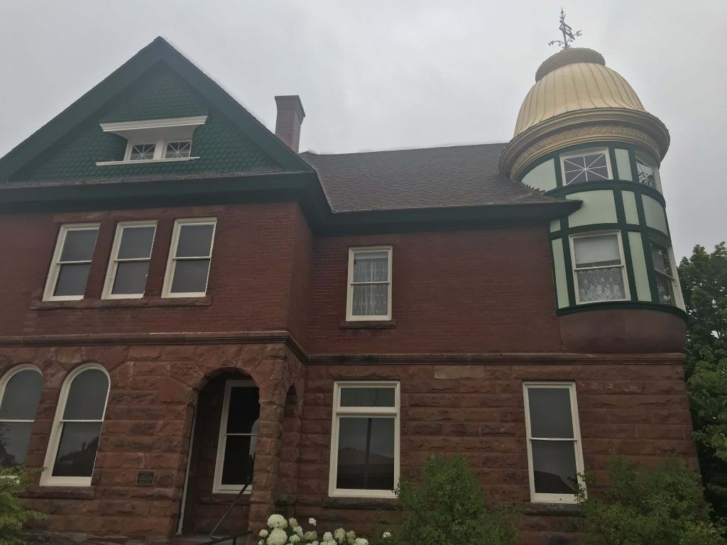 Red brick house with a green gabled roof and gold-domed turret under a cloudy sky.