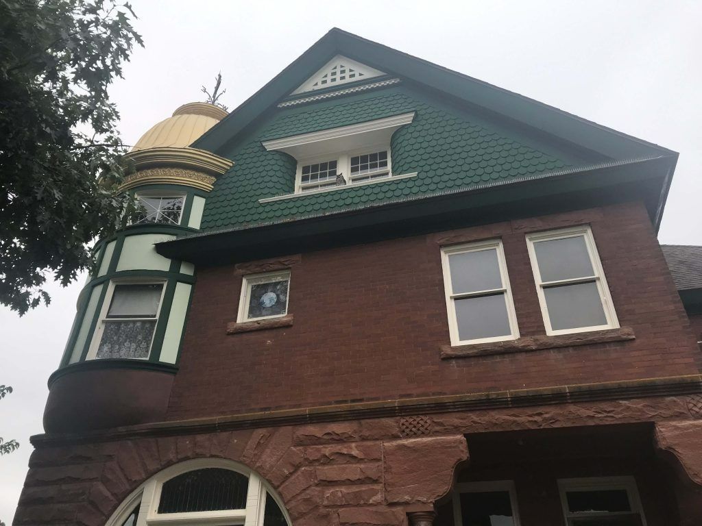 Red brick Victorian house with green and gold accents; cloudy sky.