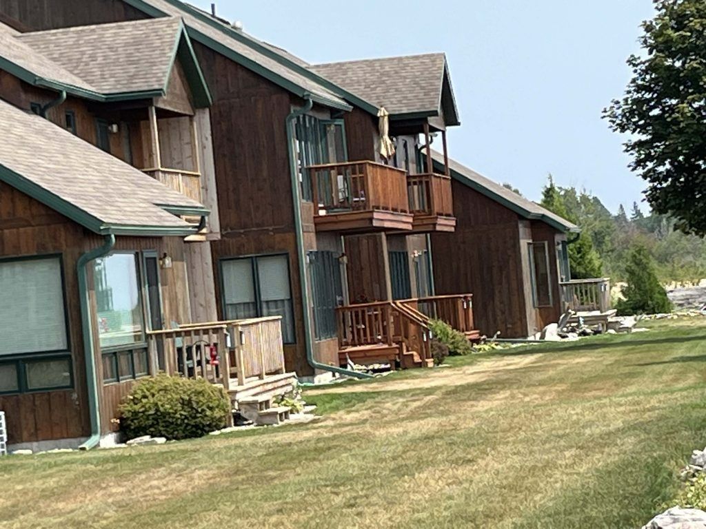 Brown wooden townhouses with balconies, surrounded by green grass under a clear sky.