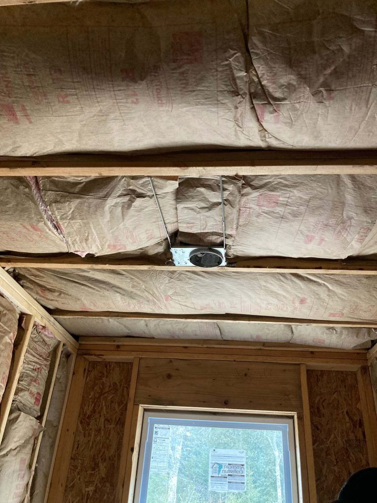 Interior view of a framed room under construction with insulation, exposed beams, and a vent in the ceiling.