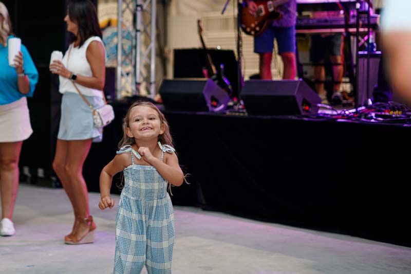 A little girl is dancing on a stage in front of a band.