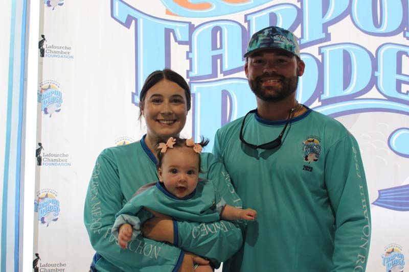 A man and a woman are holding a baby in front of a sign.