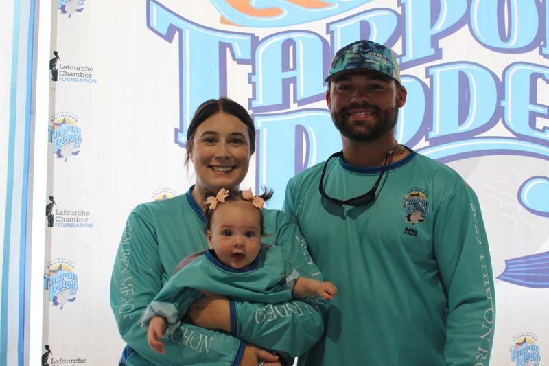 A man and a woman are holding a baby in front of a sign.