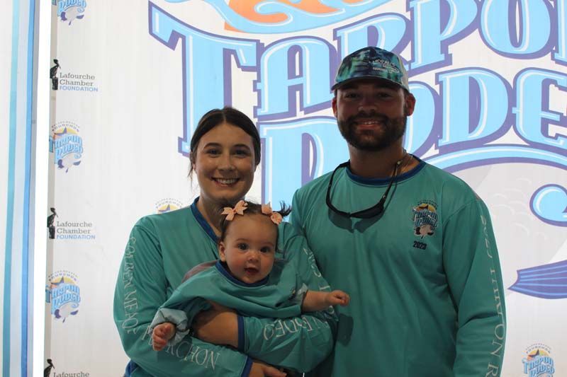 A man and woman are holding a baby in front of a sign.