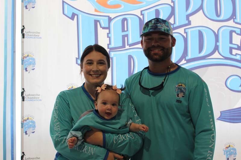 A man and woman are holding a baby in front of a sign.