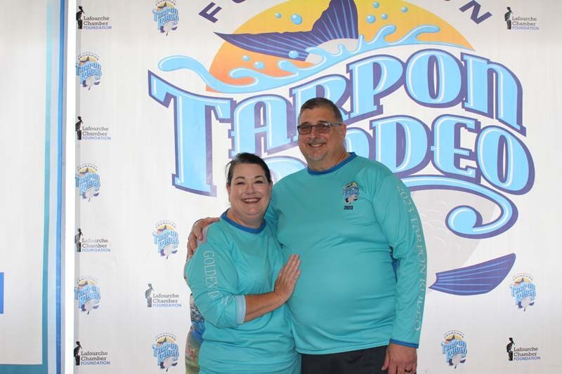 A man and a woman are posing for a picture in front of a sign that says tarpon rodeo.