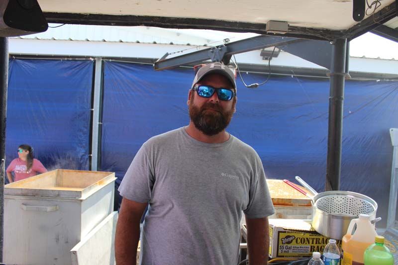 A man wearing sunglasses and a hat is standing in front of a blue curtain.