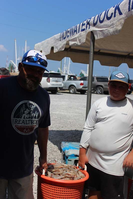 Two men are standing under a tent holding a basket of shrimp.