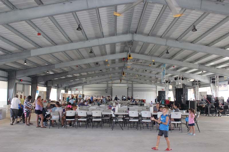 A group of people are standing in a large room with tables and chairs.