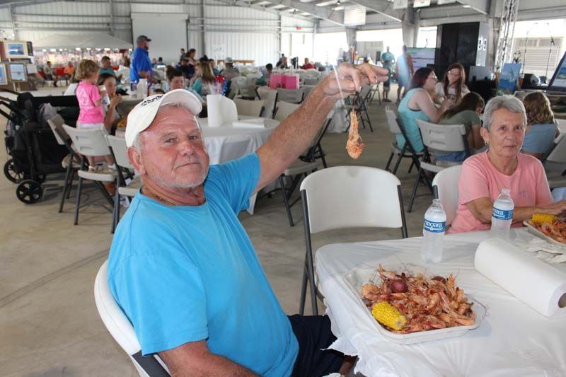 A man is sitting at a table holding a shrimp in his hand.