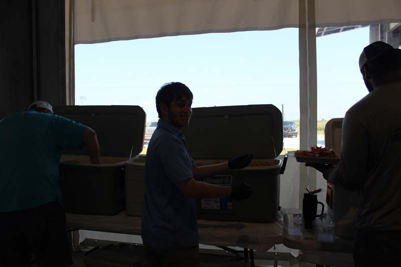 A group of people are standing around a table with coolers in front of a window.