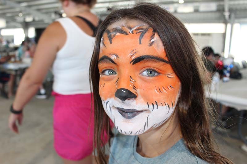 A young girl with her face painted like a tiger.