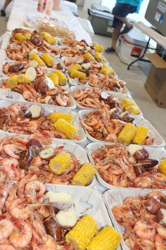 A long table topped with plates of shrimp , corn , potatoes and sausage.