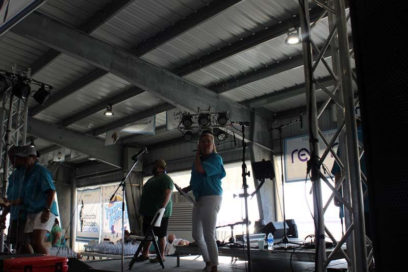 A woman in a blue shirt is standing on a stage talking into a microphone.