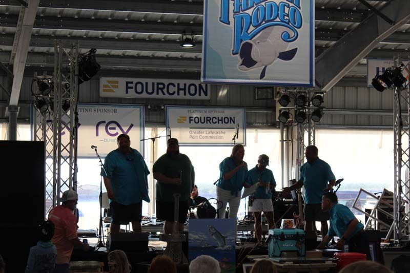 A group of people standing on a stage under a sign that says fourchon