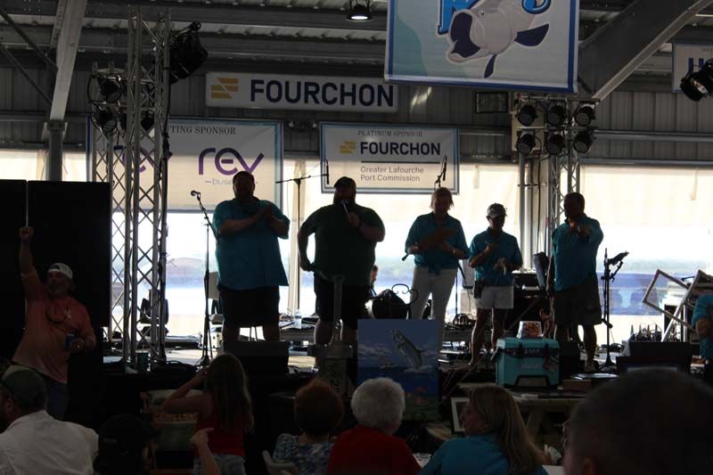 A group of men standing on a stage under a sign that says fourchon