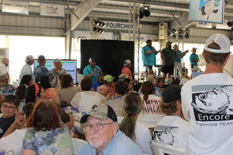 A man wearing a shirt that says encore fishing is standing in front of a crowd of people