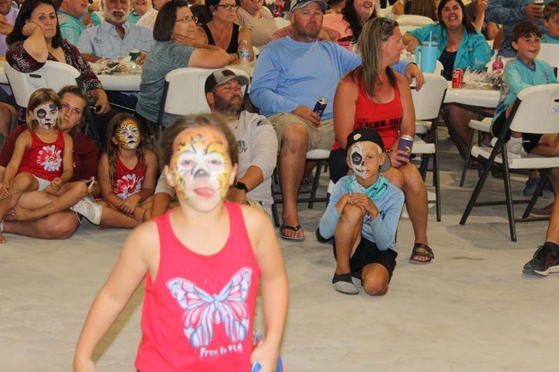 A girl with a butterfly on her shirt is running in front of a crowd of people.