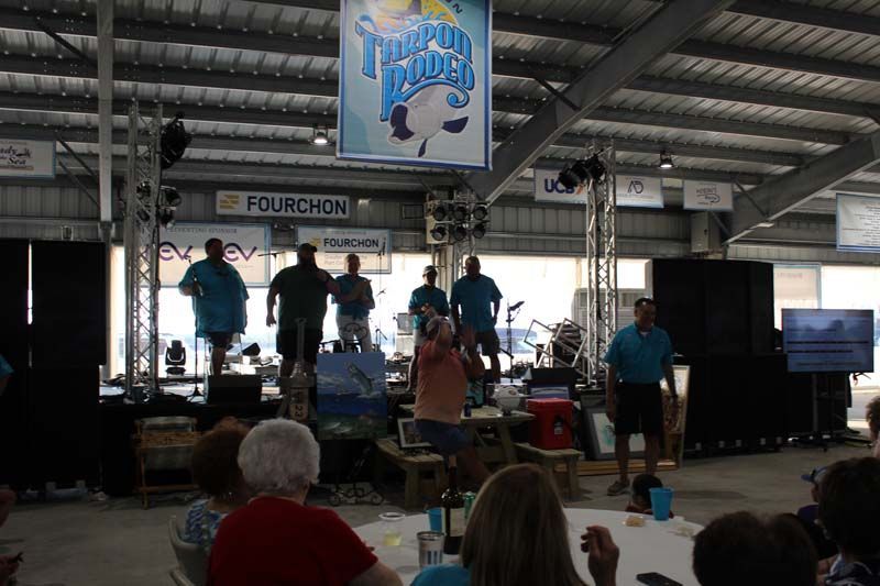 A group of people are sitting at a table in front of a stage with a sign that says fourchon