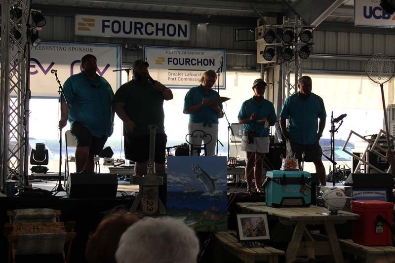 A group of men are standing on a stage in front of a sign that says fourchon