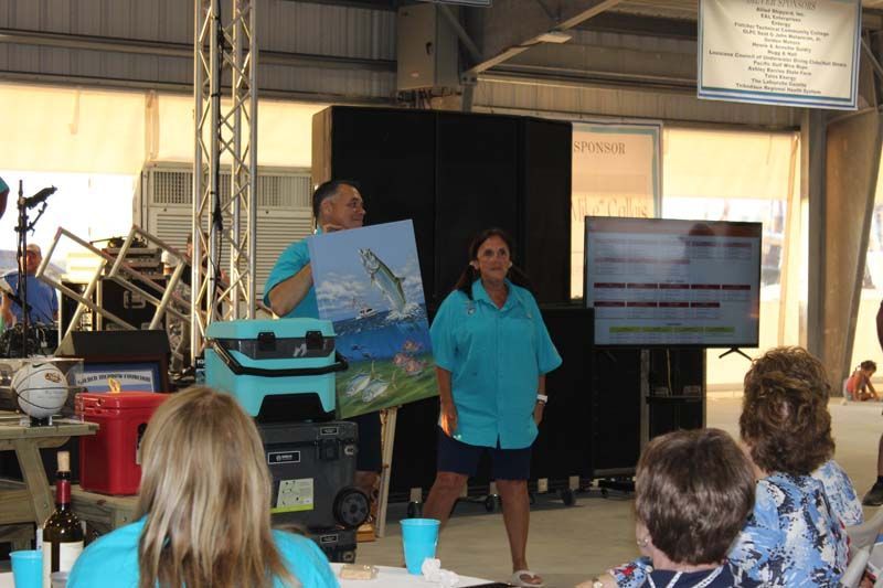 A man is holding a painting of a fish while a woman holds a cooler