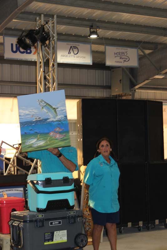 A woman in a blue shirt is holding a painting of a fish