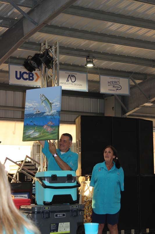A man is holding up a painting of a fish in front of a sign that says ucb
