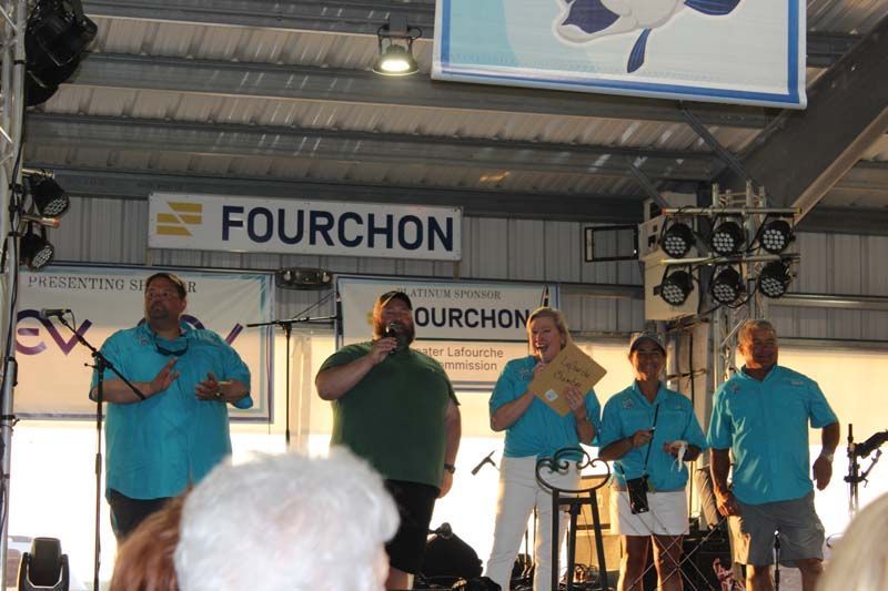A group of people standing on a stage under a sign that says fourchon