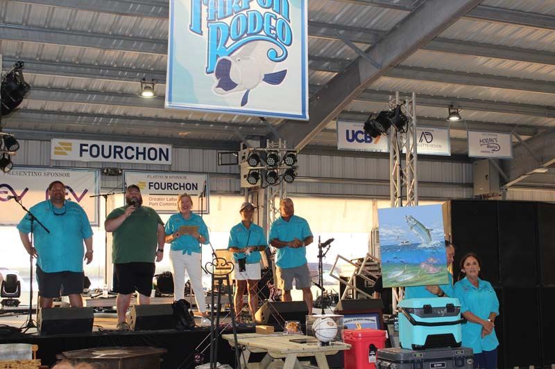 A group of people are standing on a stage in front of a sign that says fourchon