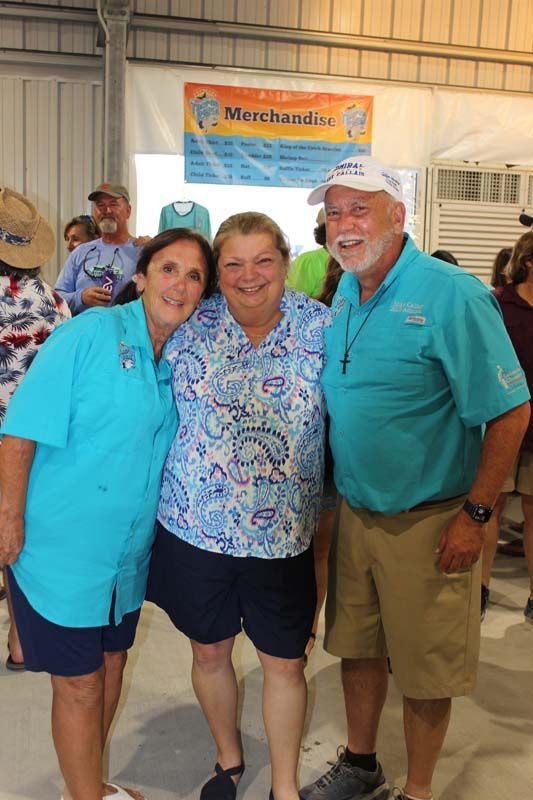 Three people are posing for a picture in front of a sign that says merchants.