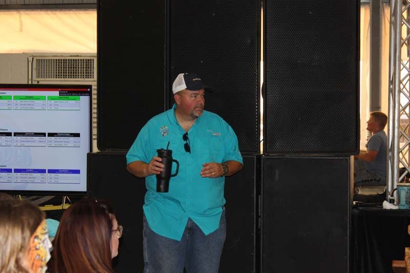 A man is standing in front of a group of people holding a cup.
