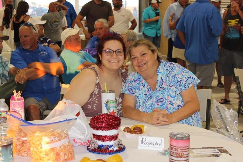 Two women are sitting at a table in front of a crowd of people.