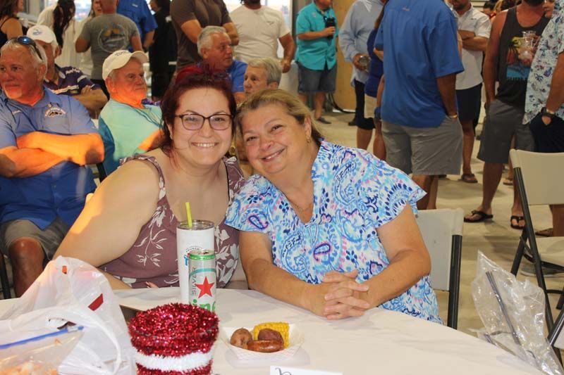 Two women are sitting at a table in front of a crowd of people.