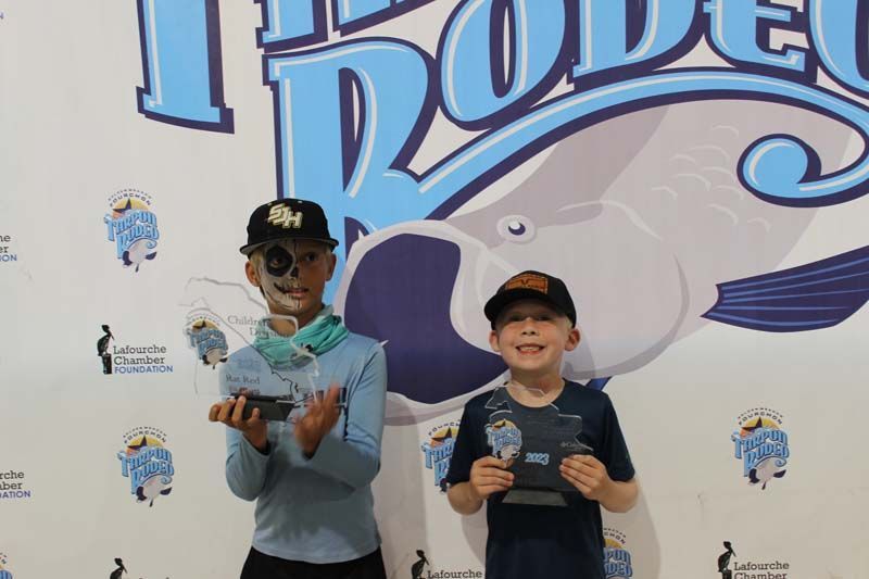 Two young boys are standing in front of a wall holding trophies.