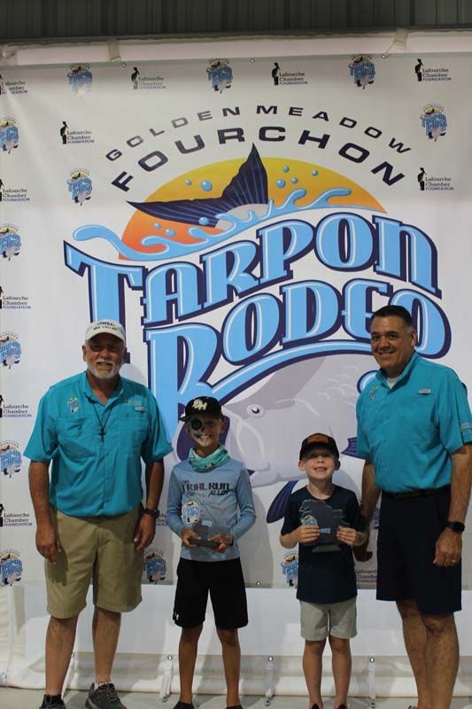 A group of people standing in front of a tarpon rodeo banner