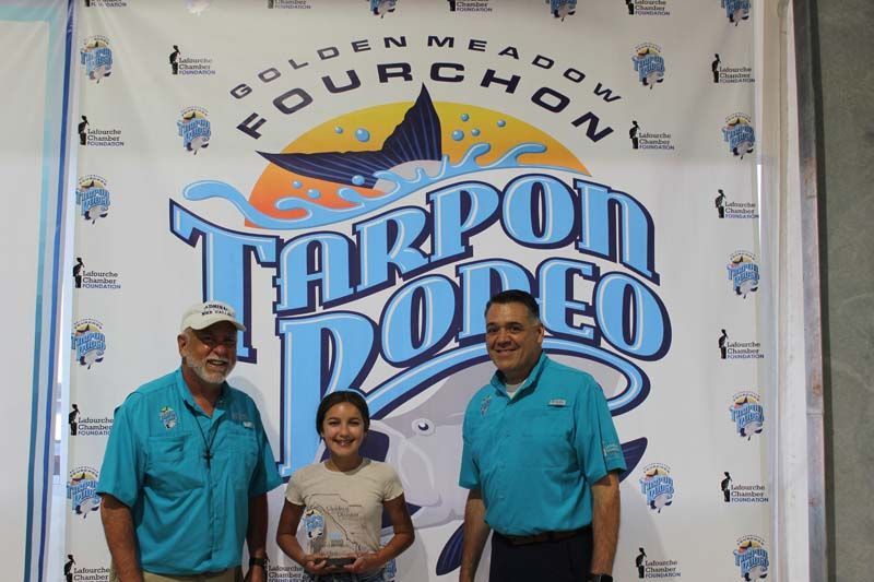 Three people standing in front of a tarpon rodeo banner