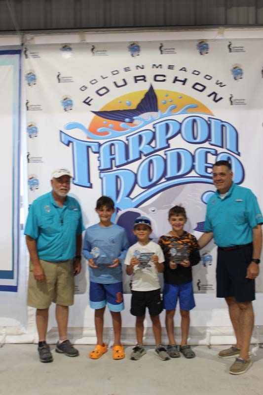 A group of people standing in front of a tarpon rodeo banner