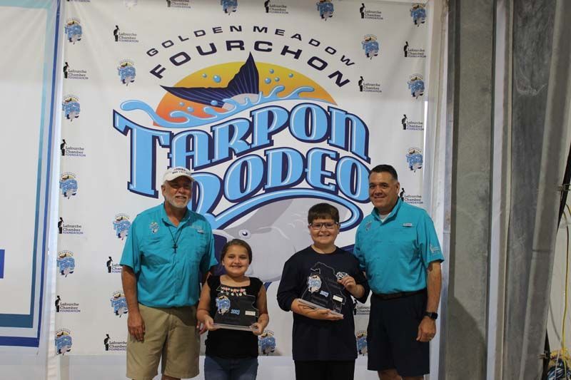 A group of people standing in front of a tarpon rodeo banner