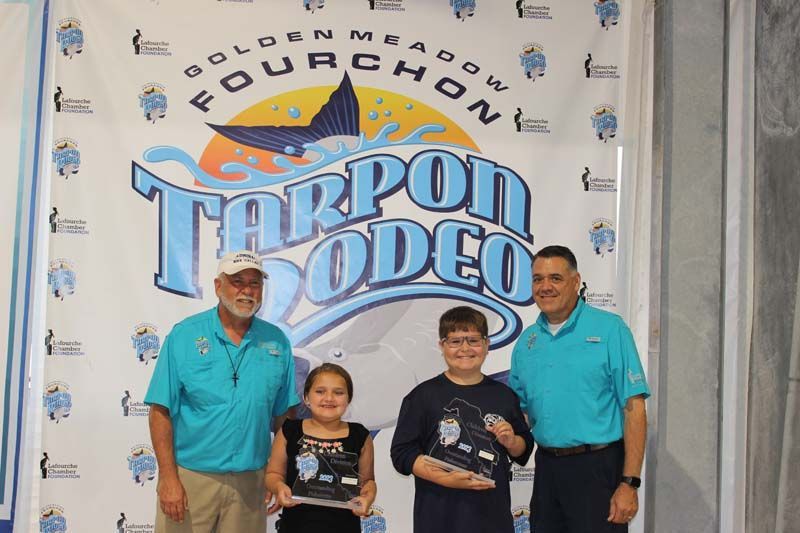 A group of people standing in front of a tarpon rodeo banner.