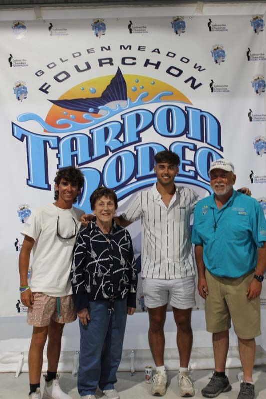 A group of people standing in front of a tarpon rodeo banner