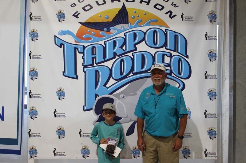A man and a boy standing in front of a tarpon rodeo banner