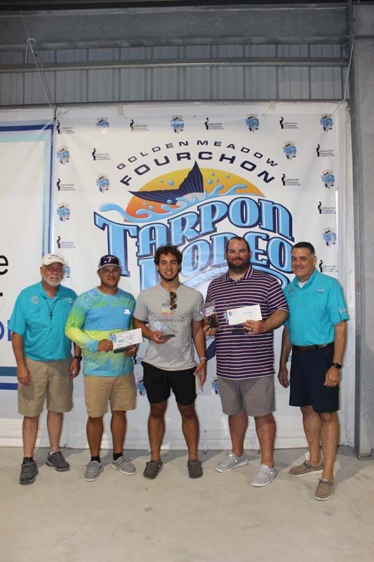 A group of men are posing for a picture in front of a tarpon tournament banner.