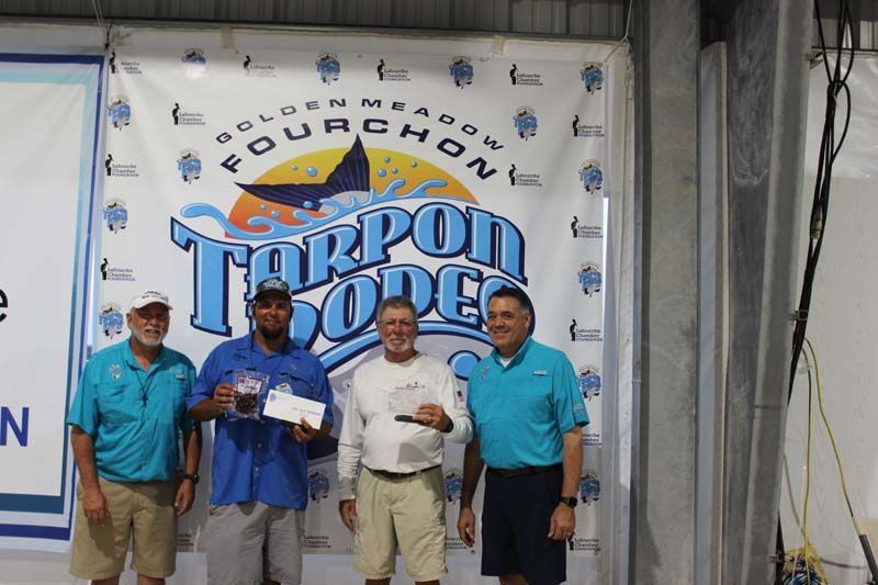 A group of men standing in front of a tarpon rodeo banner
