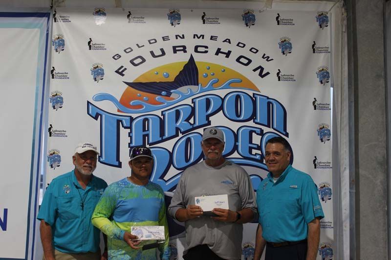 A group of men standing in front of a tarpon rodeo banner