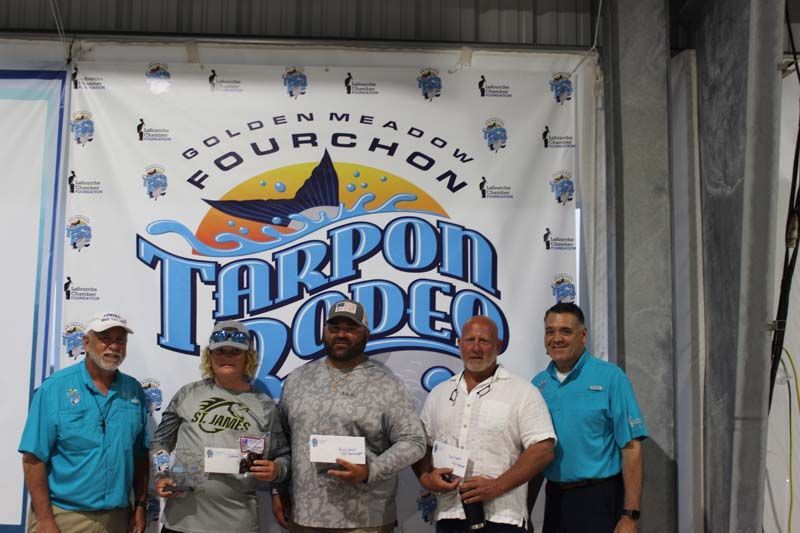A group of men standing in front of a tarpon rodeo banner