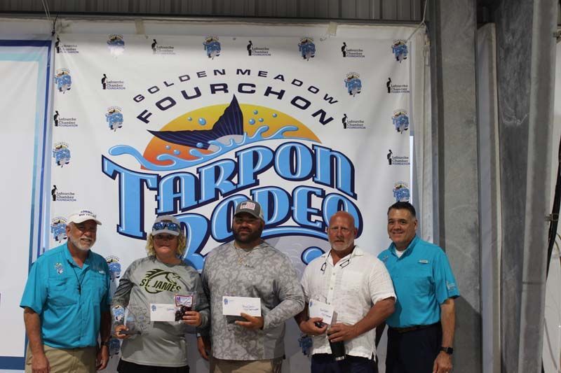 A group of people standing in front of a tarpon rodeo banner