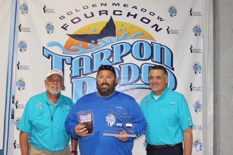 Three men are posing for a picture in front of a tarpon doo banner.