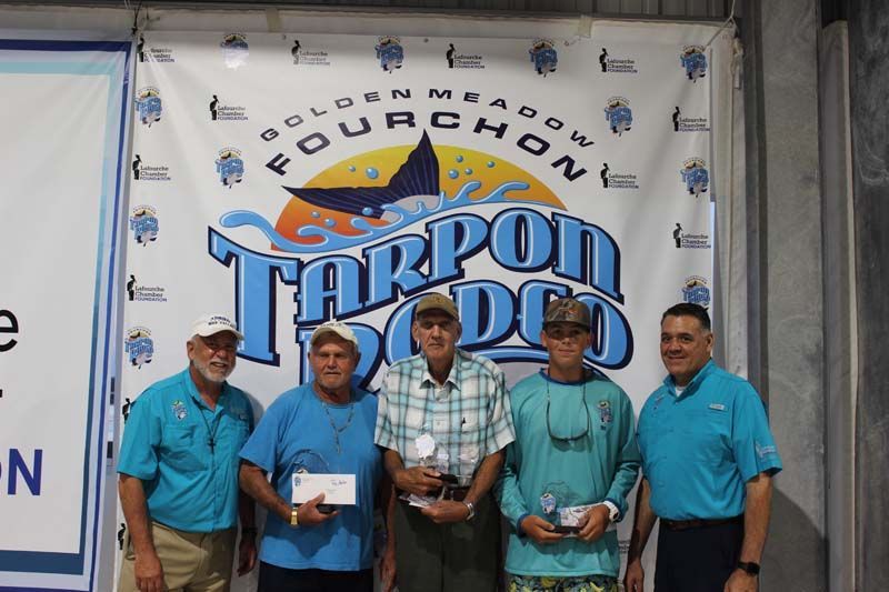 A group of men standing in front of a tarpon rodeo banner