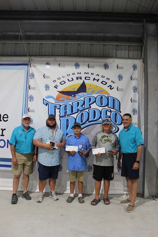 A group of men are standing in front of a tarpon rodeo banner.